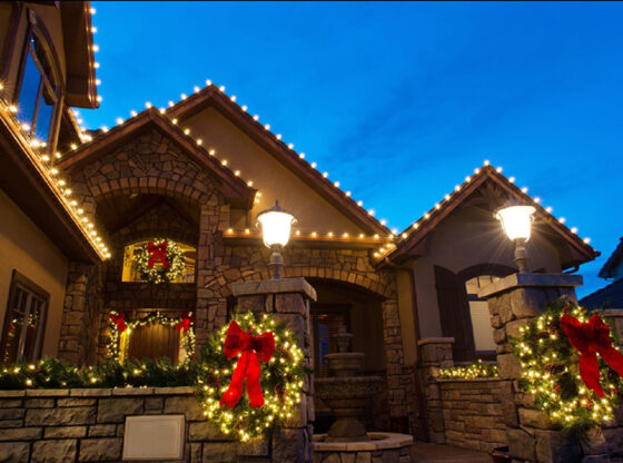 stone and stucco home with holiday lighting, bows and garlands