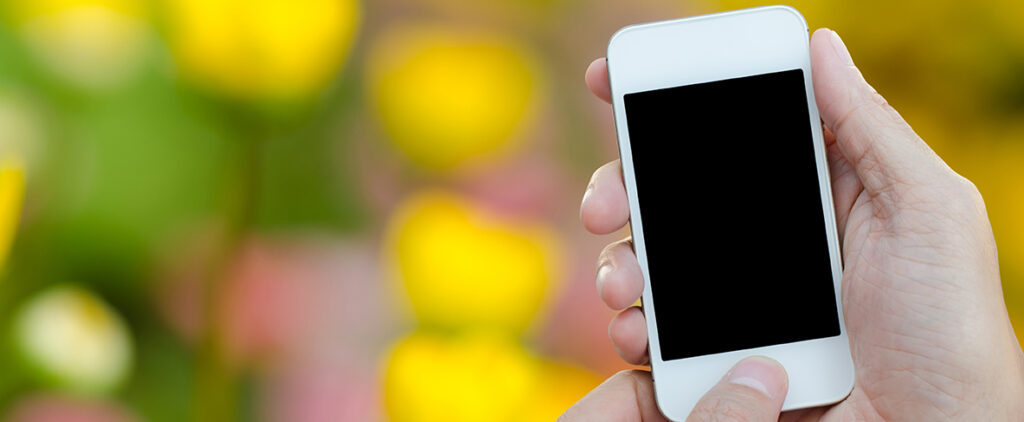 Man hand hold and touch screen smart phone, tablet,cellphone over blurred colorful flowers background.