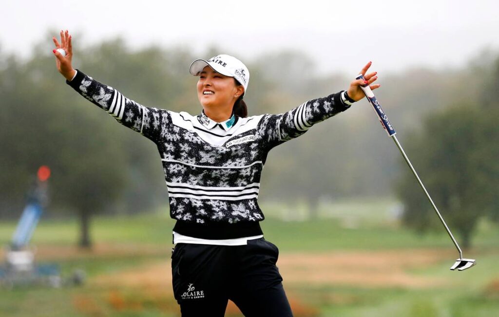 A woman golf player with her arms up in the air, victorious.